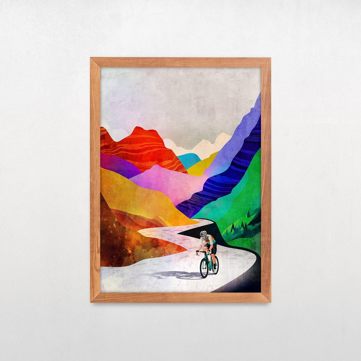 A framed abstract wall art print showing a cyclist on a winding road with colorful mountain layers