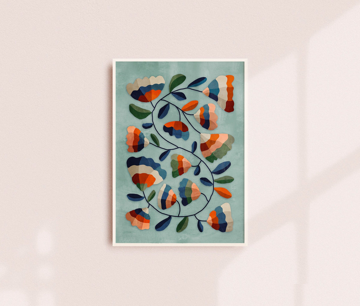 Art print featuring an abstract floral pattern in orange, navy, green, and cream on a light teal background, displayed on a soft pink wall with a subtle shadow.