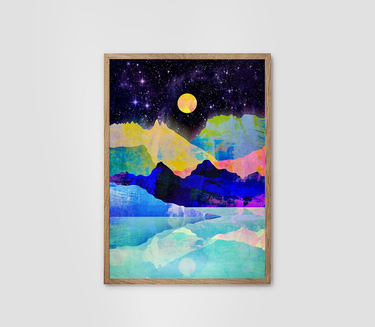 A framed abstract landscape art print featuring a starry night sky, a yellow moon, colorful mountains, and icy water, displayed on a light gray wall.