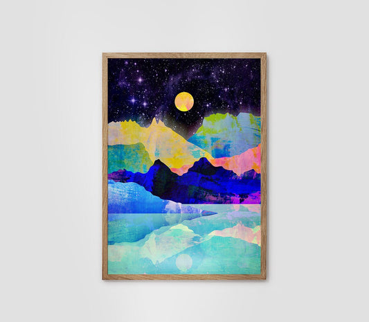 A framed abstract landscape art print featuring a starry night sky, a yellow moon, colorful mountains, and icy water, displayed on a light gray wall.