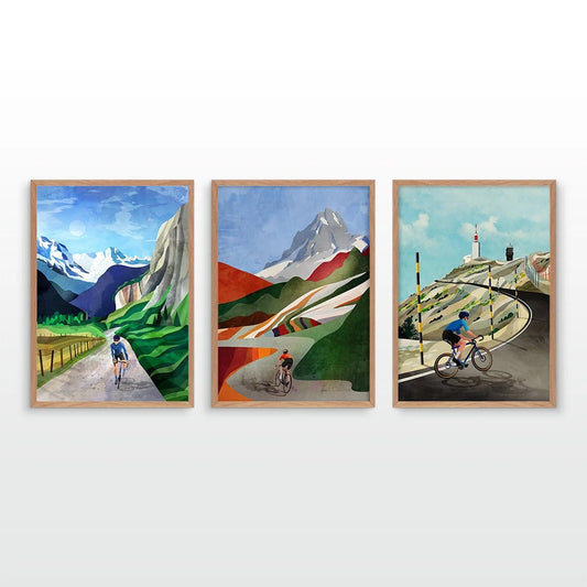 A set of three framed art prints depicting stylized mountain landscapes with cyclists, displayed side-by-side on a light gray wall.