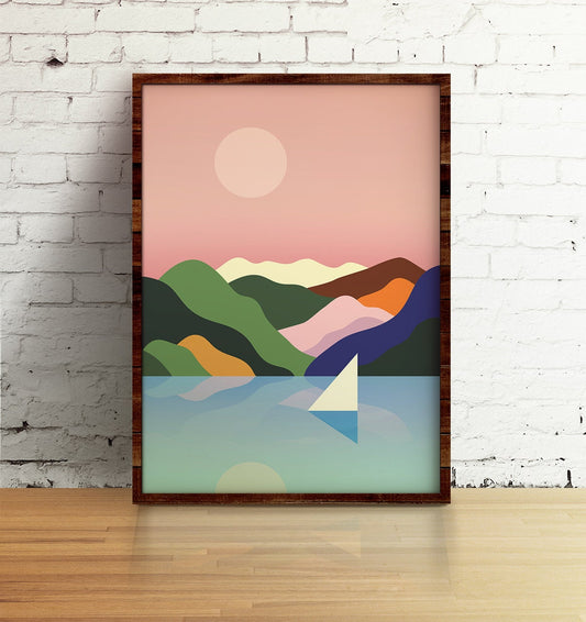 A framed minimalist art print depicting a stylized landscape with green and purple mountains, a pink sky, a sun, and a sailboat on blue water, leaning against a white brick wall on a wooden floor.