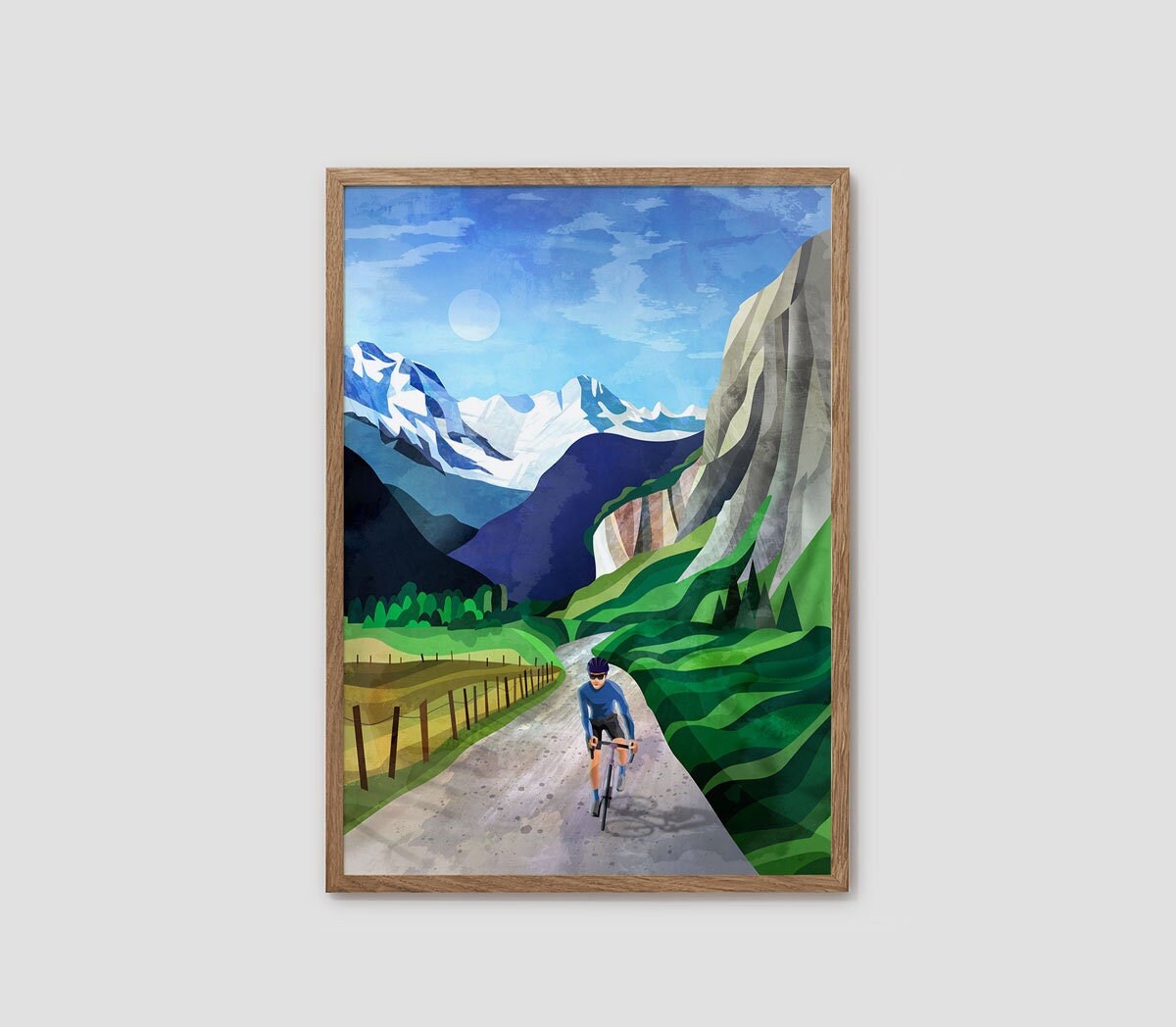 A framed art print depicting a cyclist riding along a path between green hills and snow-capped mountains under a blue sky, shown against a light gray background.