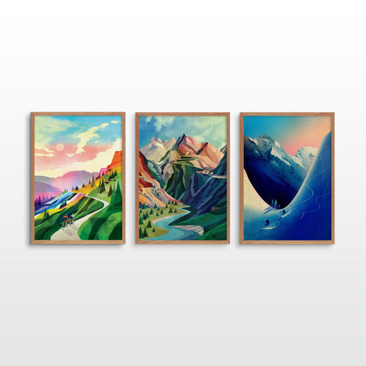 Three art prints depicting colorful mountain landscapes hang side by side on a light gray wall. The left print shows a green hillside with winding roads and distant purple mountains under a pink sky.