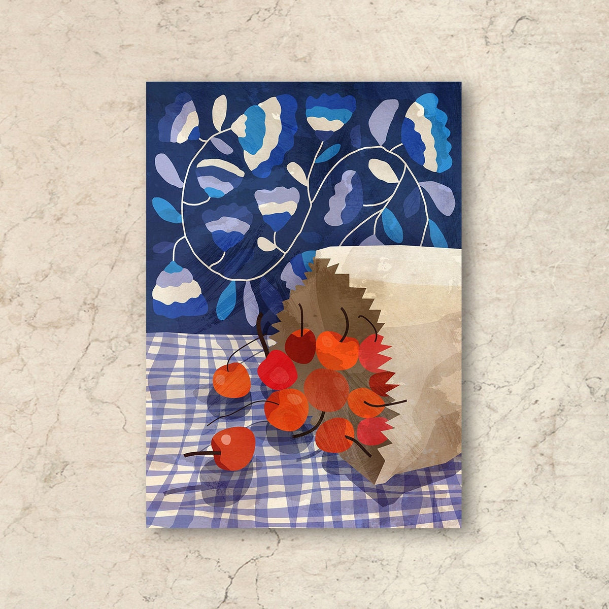 A vertical art print featuring a stylized still life of red cherries spilling from a brown paper bag onto a blue-and-white checkered tablecloth, with a dark blue floral background, displayed against a textured beige wall.