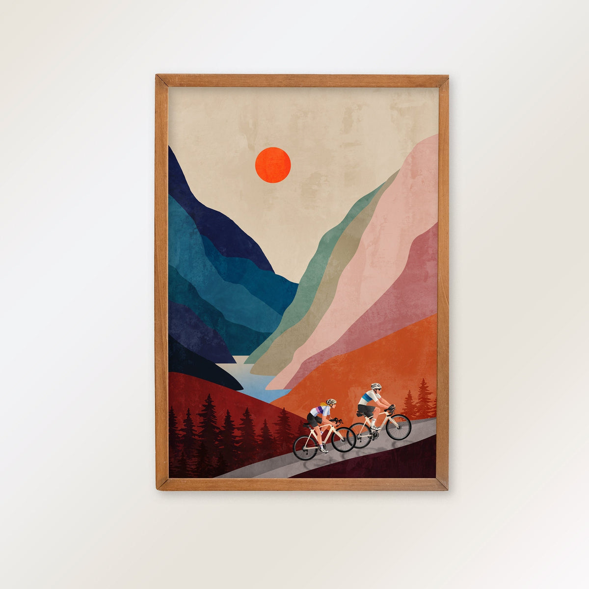 Art print featuring a stylized mountain landscape with two cyclists on a road below, hanging on a plain light wall.