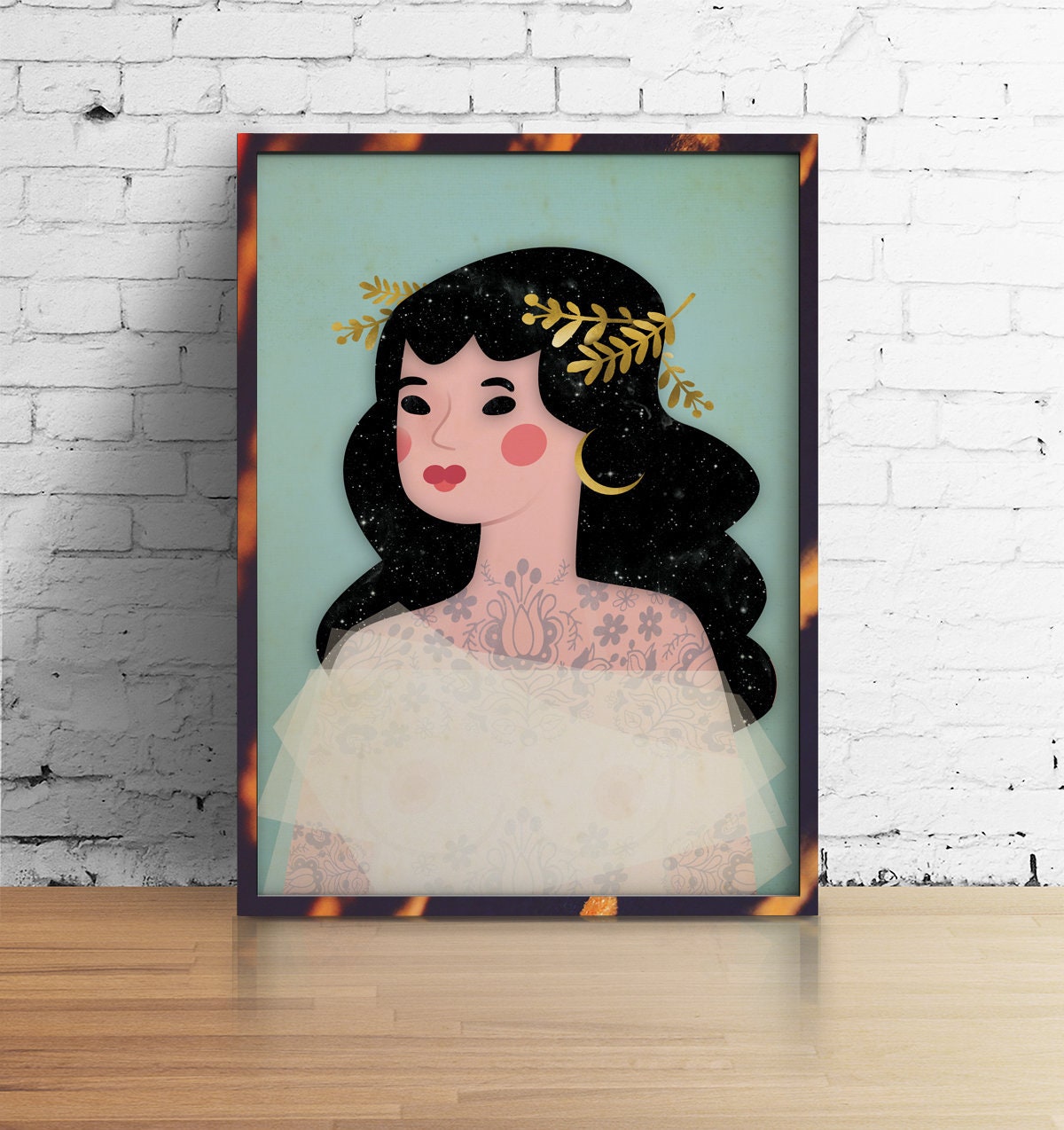 A framed art print featuring a stylized illustration of a woman with black hair, a gold leaf crown, and a white dress, leaning against a white brick wall on a light wood floor.