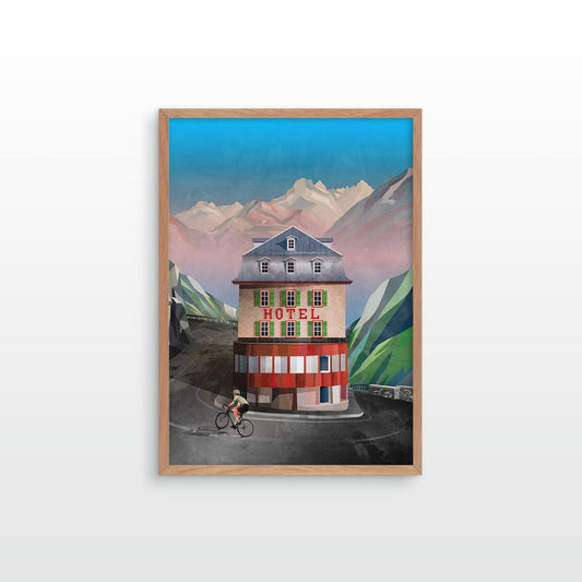 A framed art print depicting a vintage mountain hotel with a cyclist in front, set against stylized green mountains and a blue sky, displayed on a light gray wall.