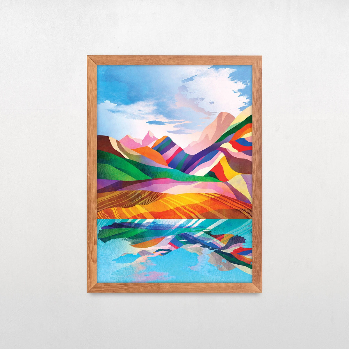 A framed art print featuring a colorful, stylized landscape with mountains, fields, and a reflective lake, displayed on a light gray wall.