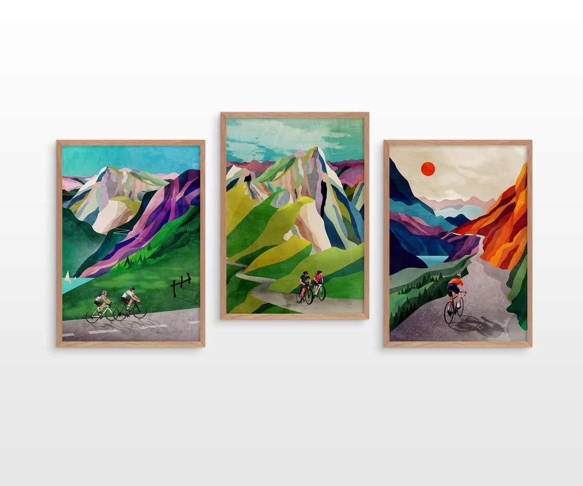 Three framed art prints depicting stylized mountain landscapes with cyclists, displayed side-by-side on a white wall.