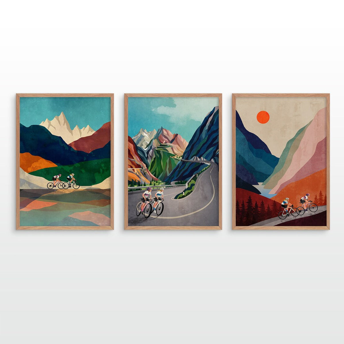 A set of three framed art prints featuring vintage-style illustrations of cyclists on winding mountain roads, displayed side-by-side on a light gray wall.