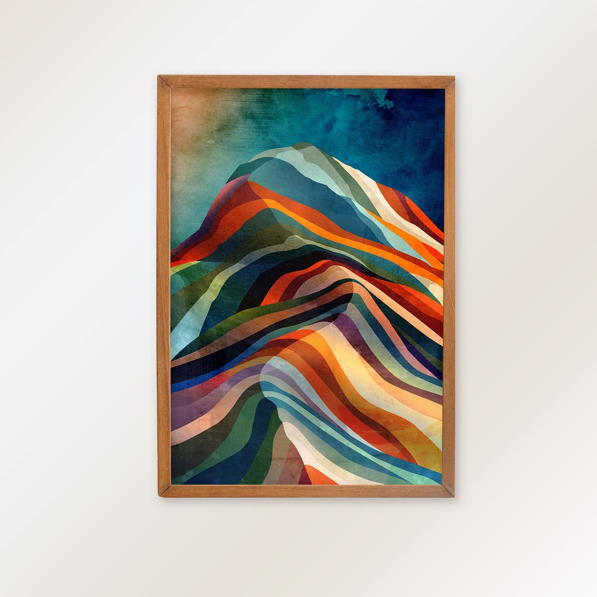 A framed abstract mountain art print with colorful layered waves in blue, green, orange, red, and cream tones, mounted on a light beige wall.