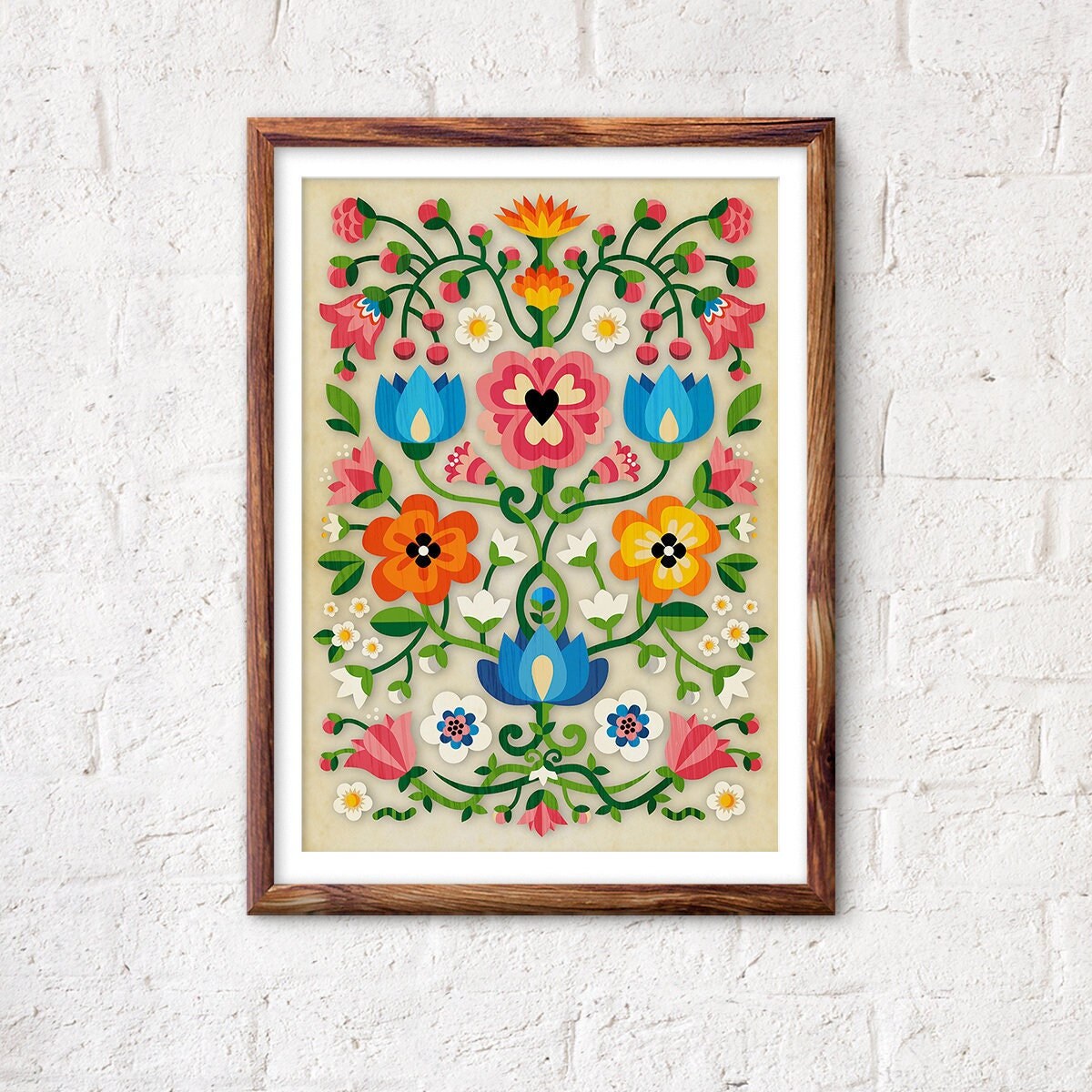 A framed folk art print featuring a colorful floral and vine pattern on a cream background, hung on a white brick wall.