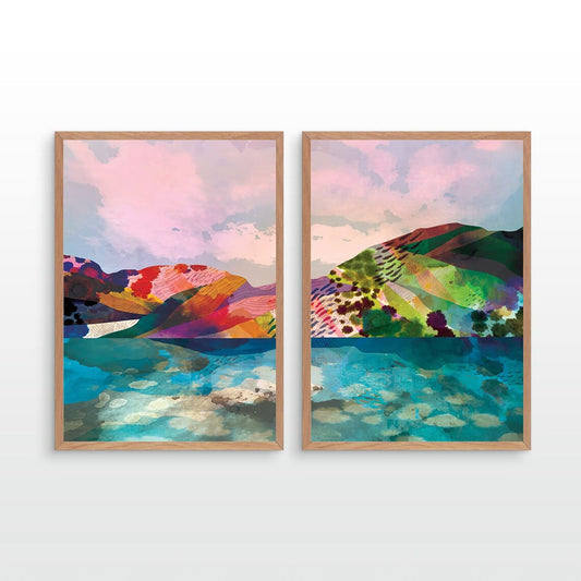 Two framed abstract landscape art prints hanging side by side on a light gray wall. The artwork features colorful hills and reflective water in pink, green, blue, red, and yellow tones