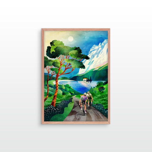 A framed art print depicting a scenic landscape with two cyclists on a road leading toward mountains and a lake, shown against a plain white background.
