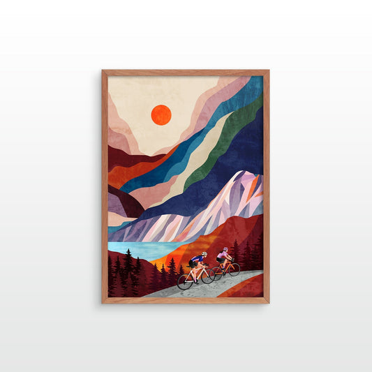 A framed art print featuring a stylized mountain landscape with two cyclists on a road, shown against a light gray background.