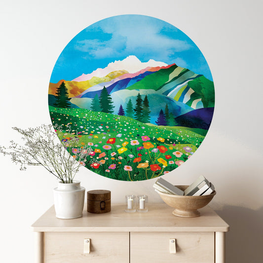 A large circular wall art print depicting a colorful mountain landscape with wildflowers