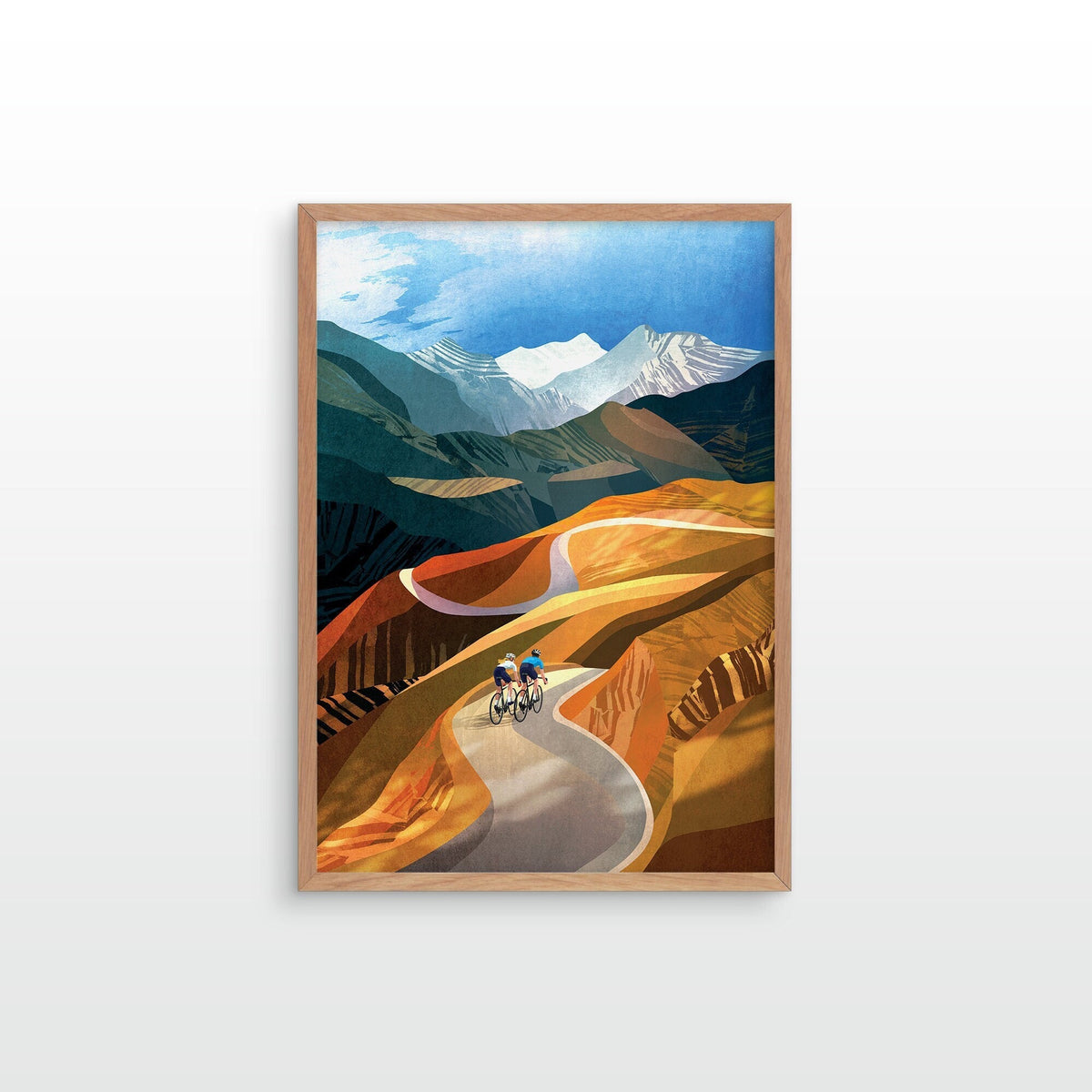 A framed art print depicting a stylized mountain landscape with a winding road and two cyclists, shown hanging on a light gray wall.