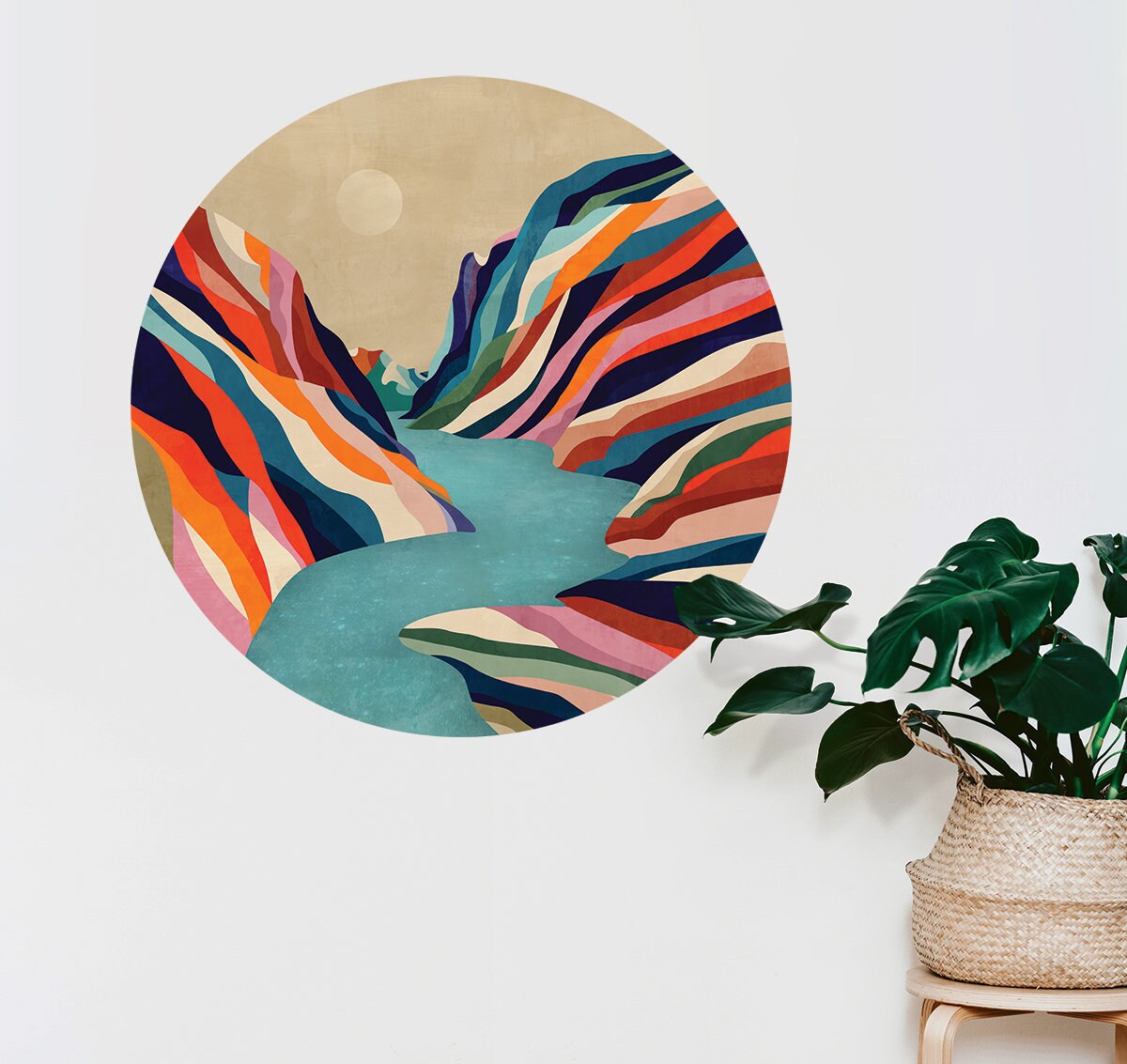 A circular wall art print featuring a colorful abstract mountain valley scene with a winding turquoise river