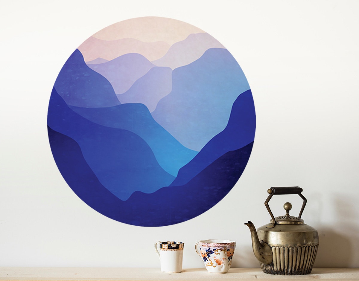 A circular wall art print featuring layered blue mountain ranges in shades of navy, royal blue, and light blue,