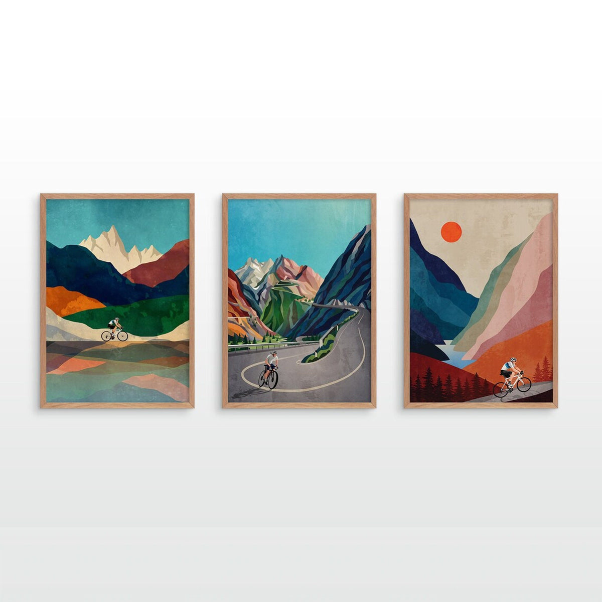 Three framed vertical art prints with a retro mountain landscape style, featuring cyclists on winding roads, displayed side-by-side on a white wall.