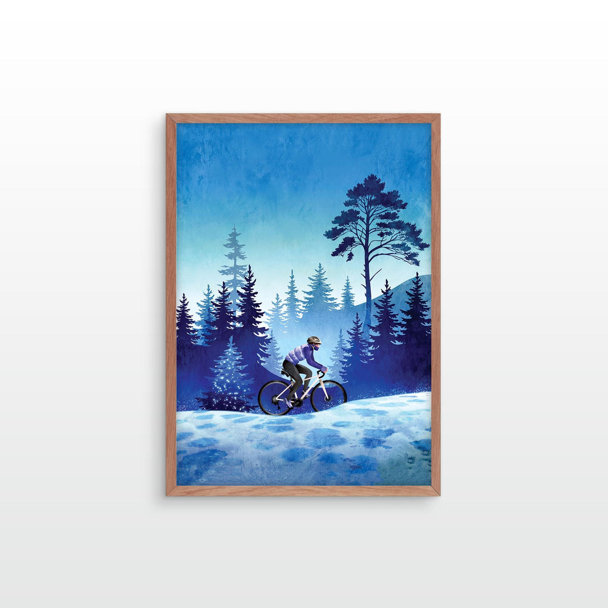 A framed art print depicting a cyclist riding through a snowy forest at night under a deep blue sky, mounted on a light gray wall.