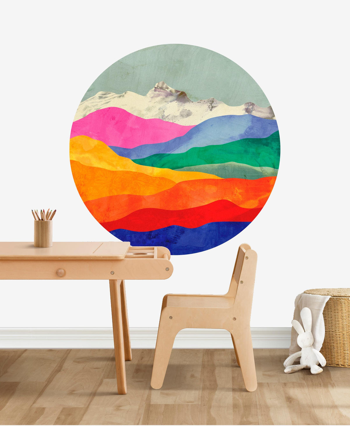 A large circular wall mural featuring a colorful watercolor mountain landscape with pink, green, blue, orange, yellow, and red layers