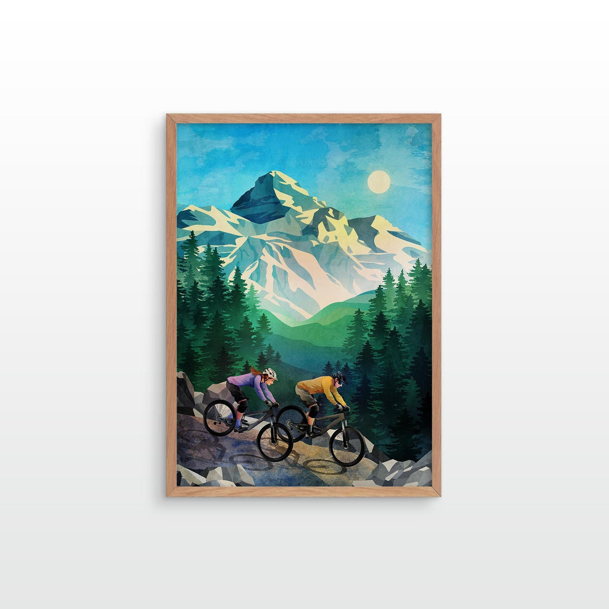 A framed art print depicting two mountain bikers on a trail with snowy mountains and pine trees under a full moon, shown against a light gray background.