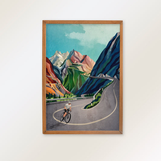 A framed art print depicting a stylized cyclist on a winding mountain road, surrounded by colorful peaks and blue-green cliffs.