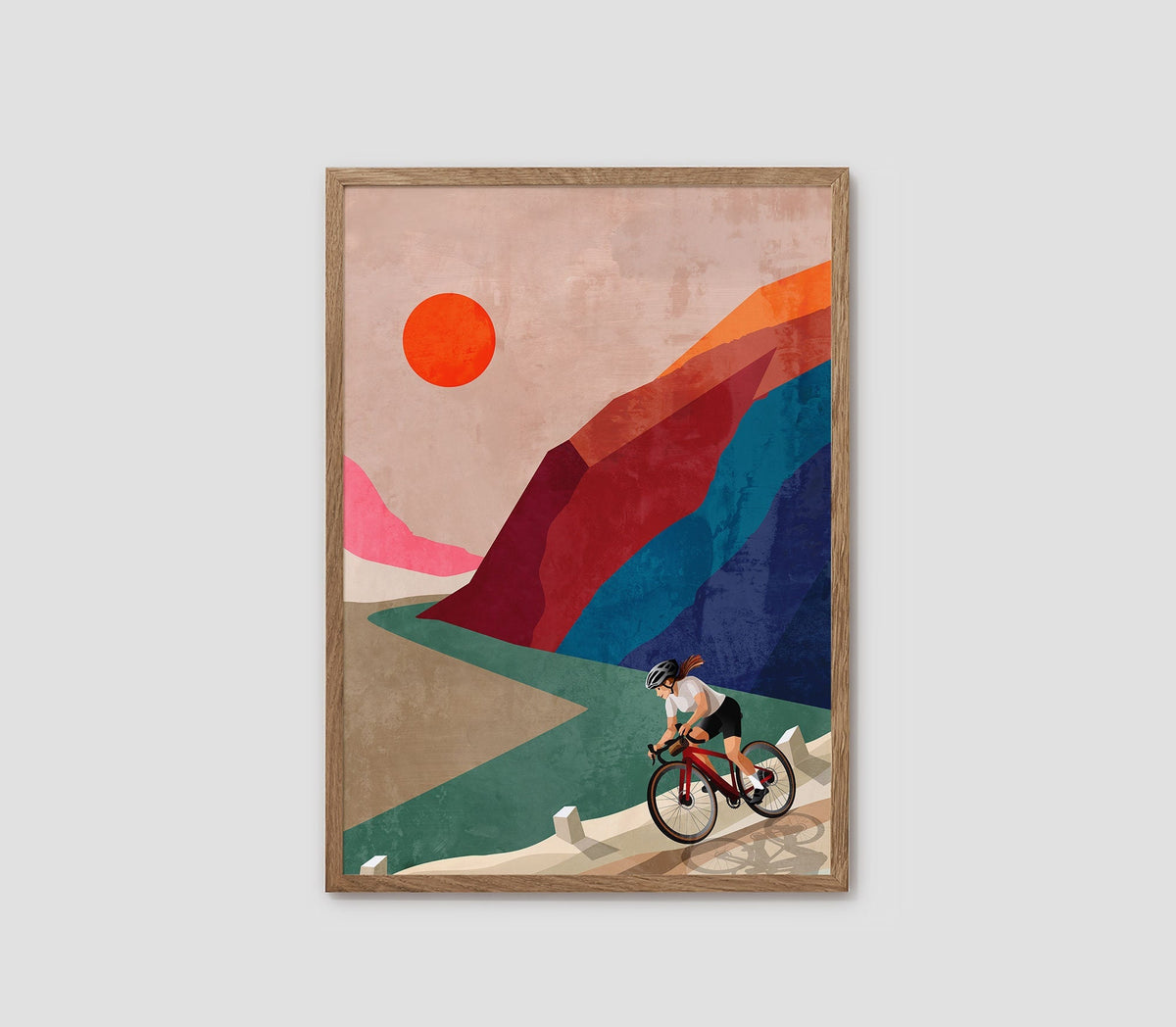 A framed art print featuring a stylized illustration of a cyclist riding along a winding path, with geometric mountains and a large orange sun in the sky, shown against a light gray background.