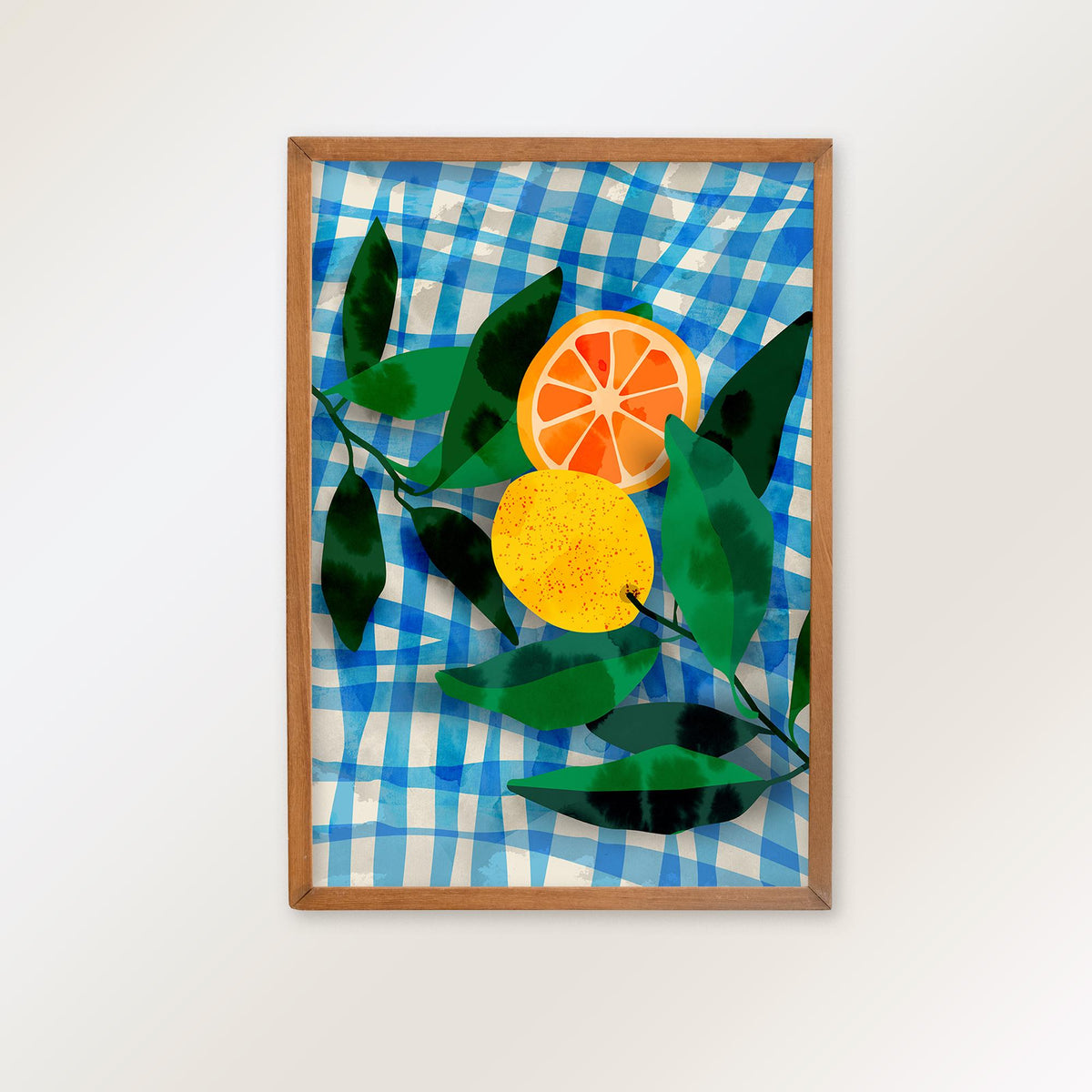 A framed art print featuring a blue and white gingham pattern background with green leaves and two citrus fruits, one sliced open to reveal orange segments.