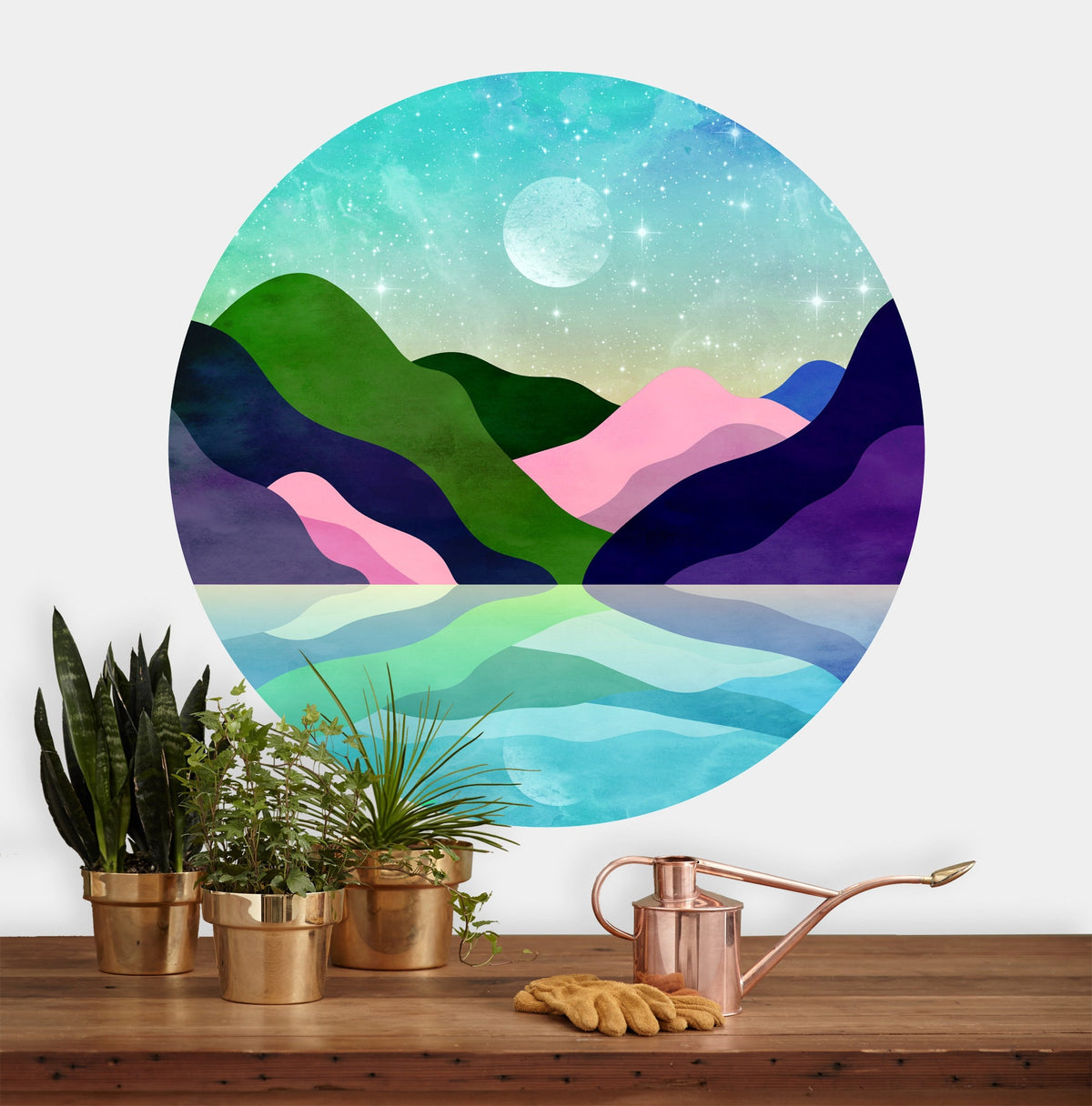A circular wall art print featuring a colorful watercolor-style landscape with green and purple mountains, pink hills, a blue lake, and a moon in the sky