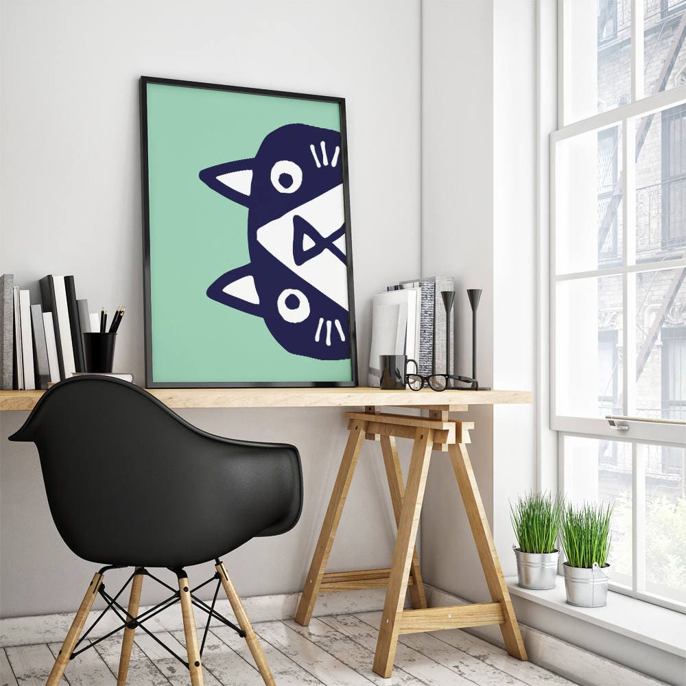 A framed minimalist art print featuring a stylized navy blue cat face on a mint green background