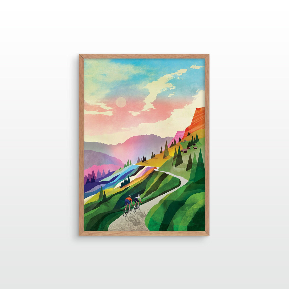 A framed art print featuring a colorful retro-style illustration of cyclists on a winding mountain road, set in a light wood frame against a white wall.